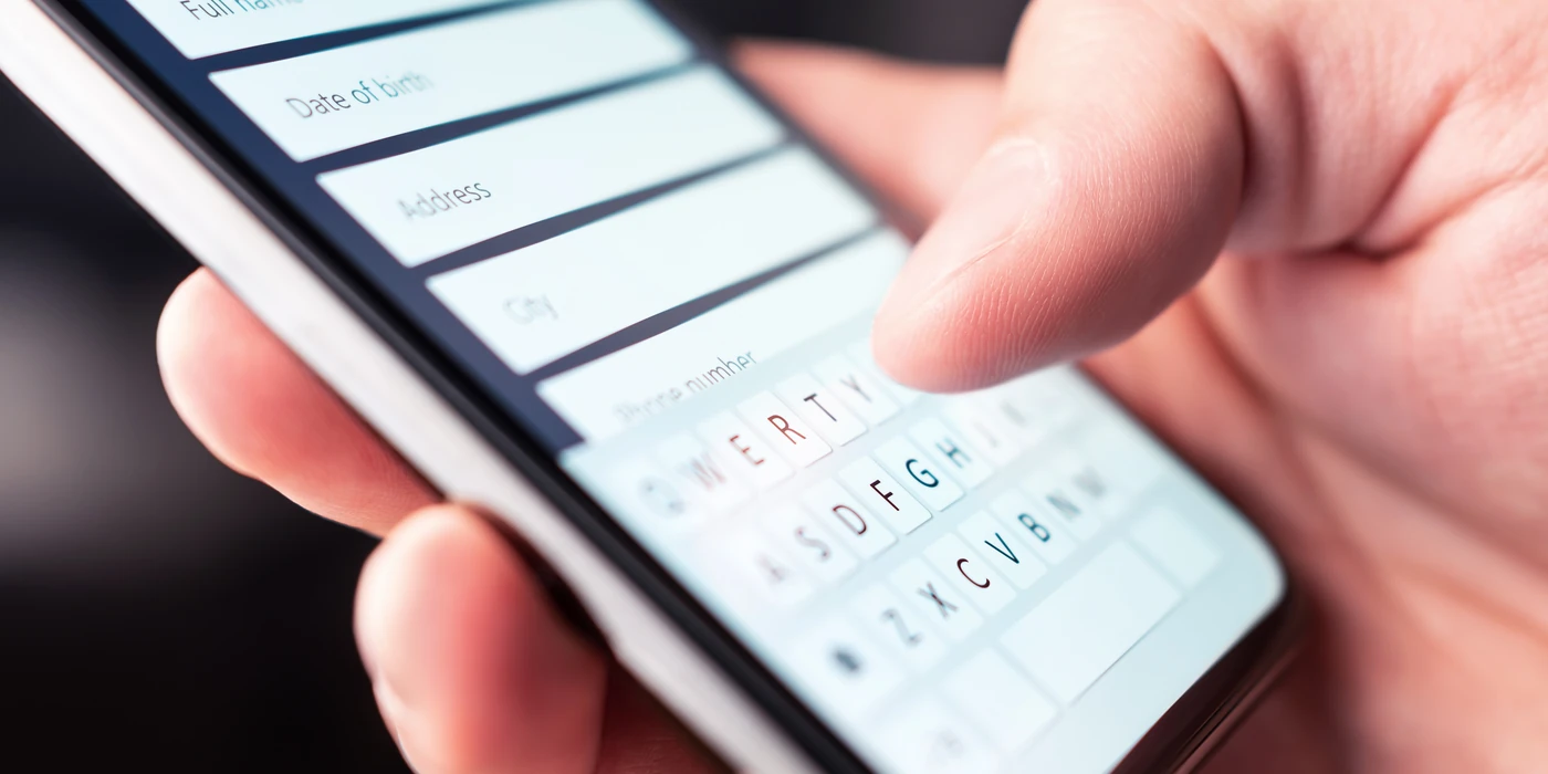 A hand holding a smartphone and filling in an online form