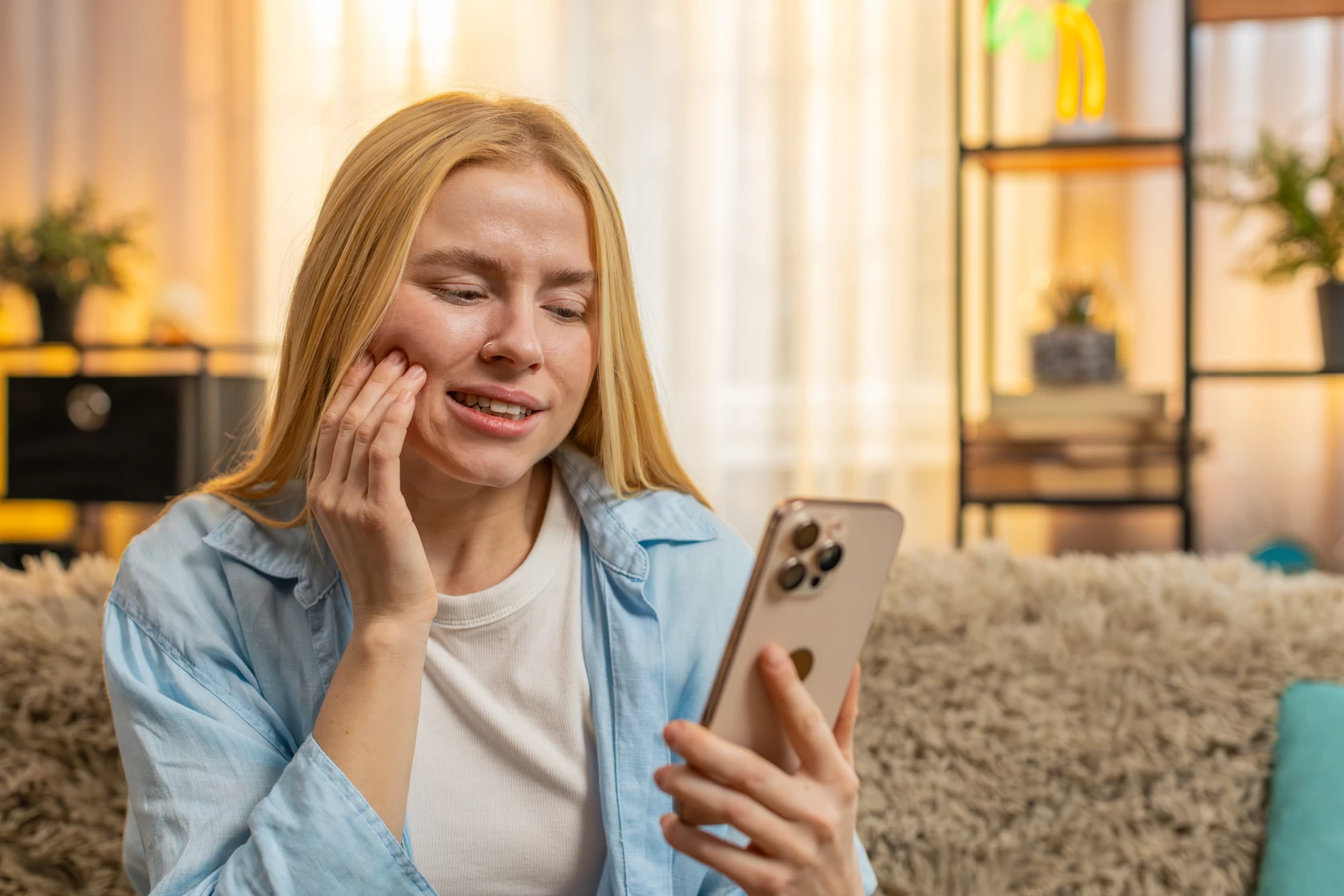 Young woman with toothache holding her cheek while looking for help on her smartphone